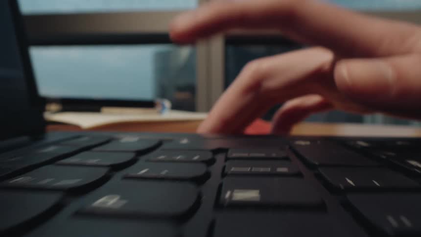 A dynamic macro shot follows a hand typing quickly across a laptop keyboard in a modern office