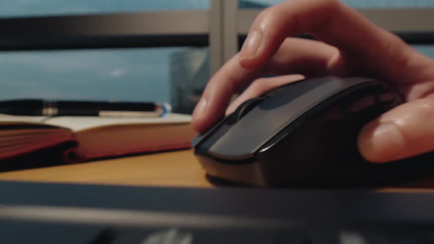 A dynamic close-up shot pushes past a laptop keyboard to a hand operating a computer mouse on a desk