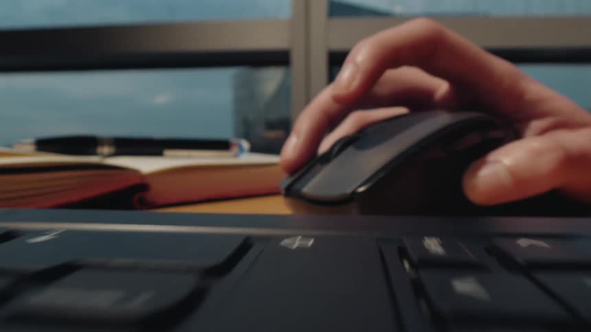 A close-up probe lens shot moves from a person typing on a laptop keyboard to using a computer mouse on a desk