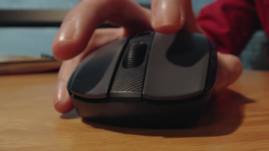 A dynamic close-up shot of a person's hand using a computer mouse, clicking and scrolling on a wooden desk