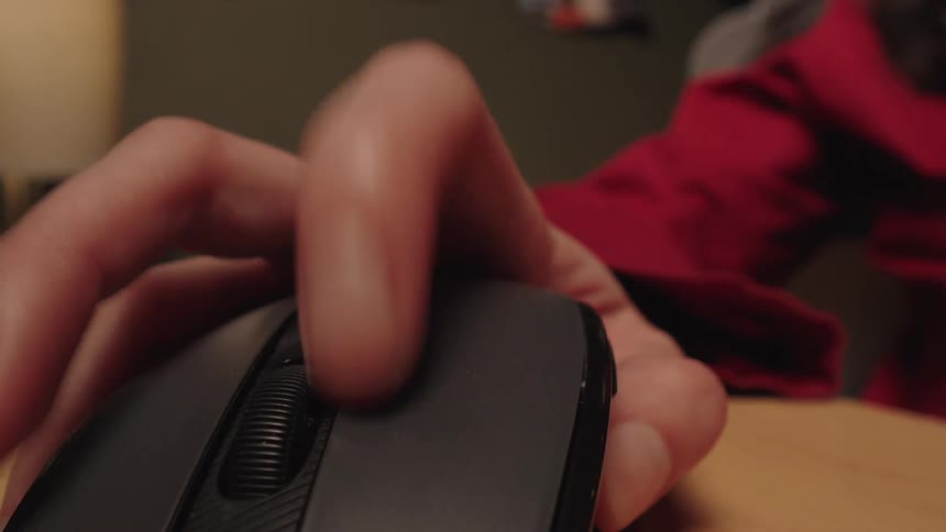 A close-up shot of a hand using a computer mouse, clicking the left button and using the scroll wheel on a wooden desk