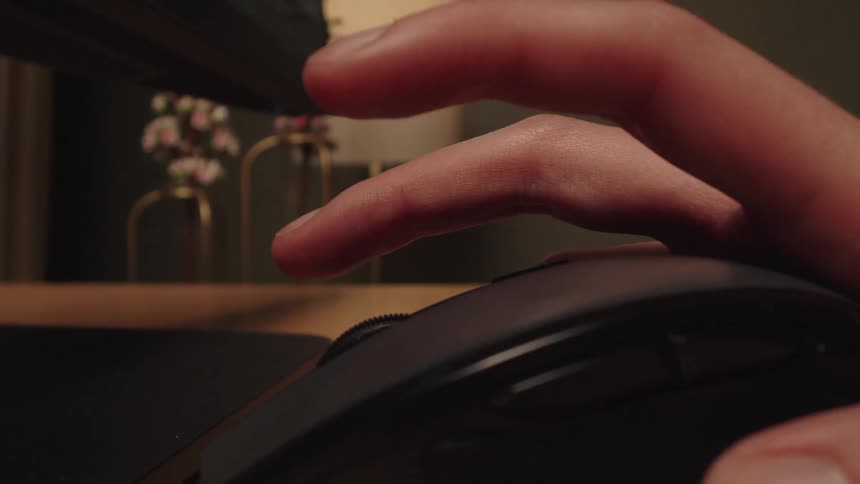 A person's hand moves into focus and begins to use the scroll wheel on a black wireless mouse at their desk