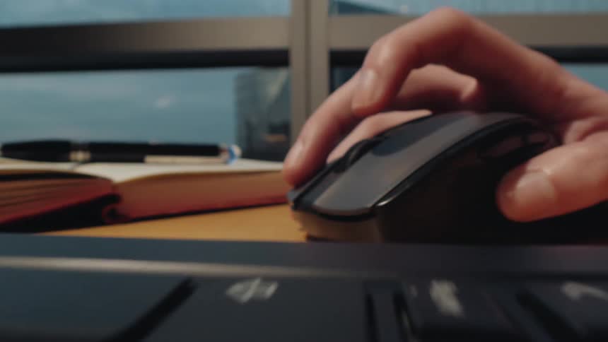 Extreme close-up dolly shot of hands typing on a laptop keyboard and using a mouse at a desk