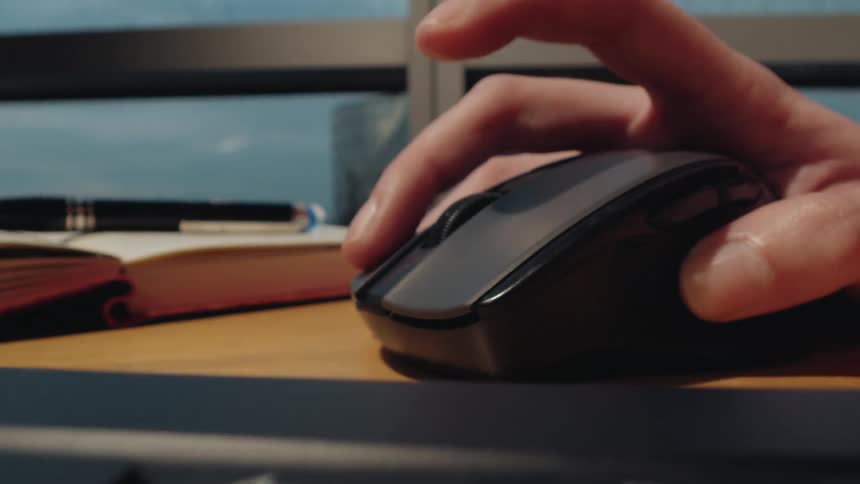 A close-up dolly shot follows a hand typing on a laptop keyboard before moving to operate a computer mouse on a desk