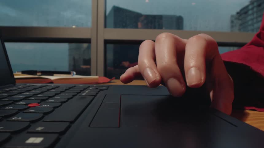 Extreme close-up of a hand typing and using the trackpad on a laptop by a window on a rainy day