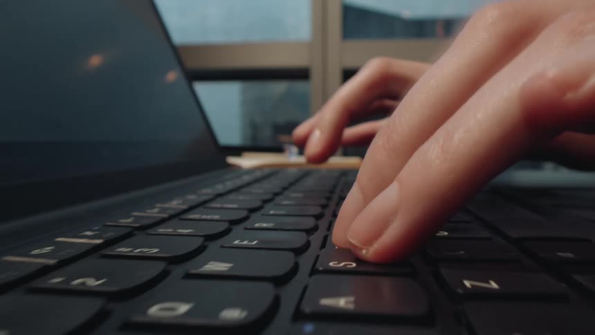 Macro probe lens pushes in on a person's hands opening a laptop and typing on the keyboard in a modern office