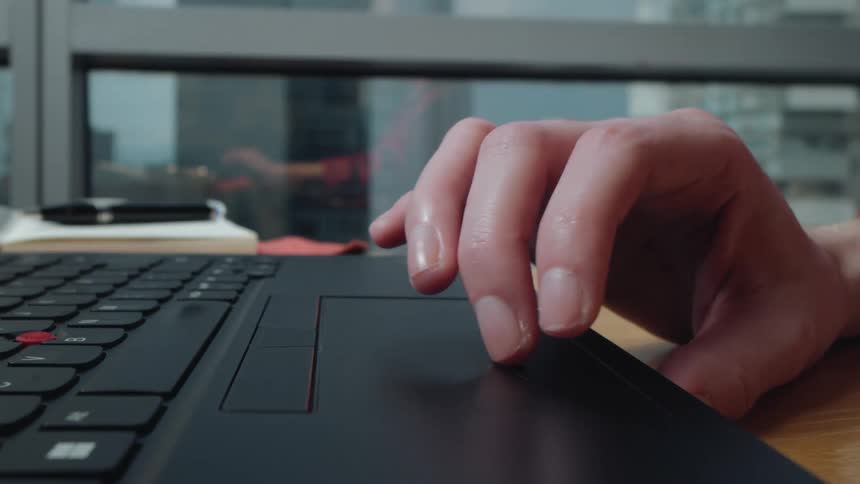 A close-up shot of a person's hand using the trackpad on a laptop computer with a city skyline in the background