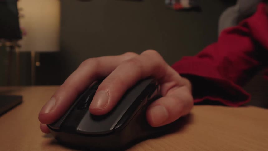 A close-up view of a person's hand using a wireless computer mouse, repeatedly clicking and scrolling the wheel on a wooden desk