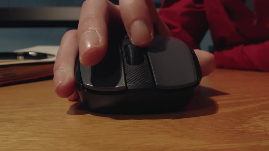 A close-up shot of a hand clicking the buttons and using the scroll wheel on a wireless computer mouse on a wooden desk