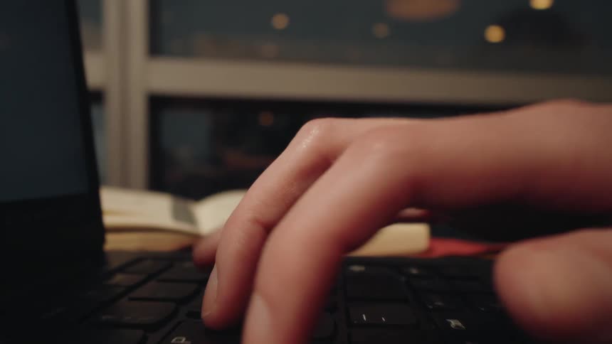 A detailed macro shot captures a person's hands typing on a laptop keyboard at night