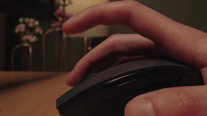 A close-up of a person's hand repeatedly clicking the left button on a wireless computer mouse on a desk