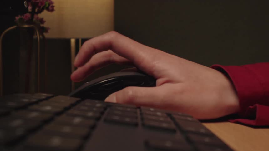 Side view close-up of a hand typing on a keyboard and clicking a mouse in a warm, dark room