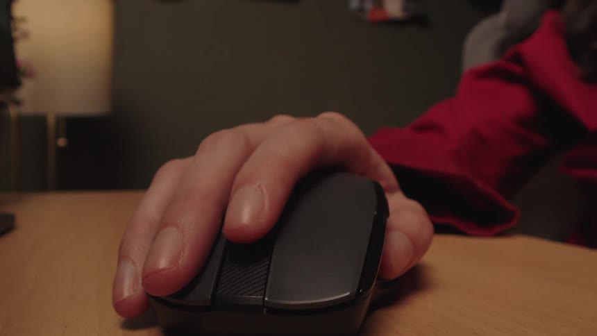 An extreme close-up of a person's hand clicking and scrolling with a wireless computer mouse on a wooden desk