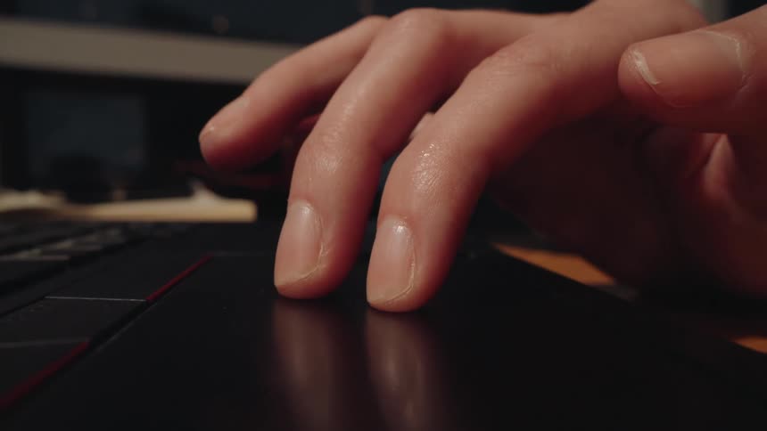 A macro close-up shot of fingers tapping and scrolling on a laptop's trackpad in a dark room at night