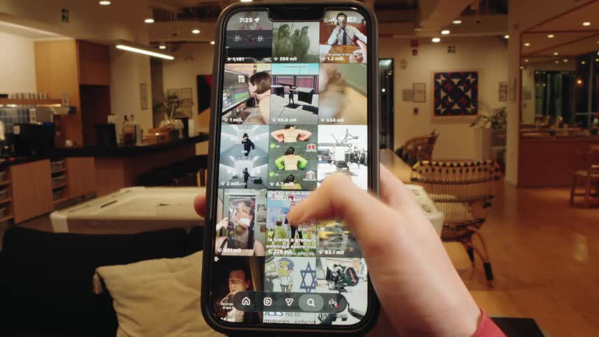 Point-of-view of a hand endlessly scrolling through a social media feed on a smartphone in a modern indoor space