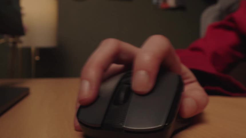 A close-up shot of a person's hand frantically and aggressively clicking a computer mouse on a wooden desk