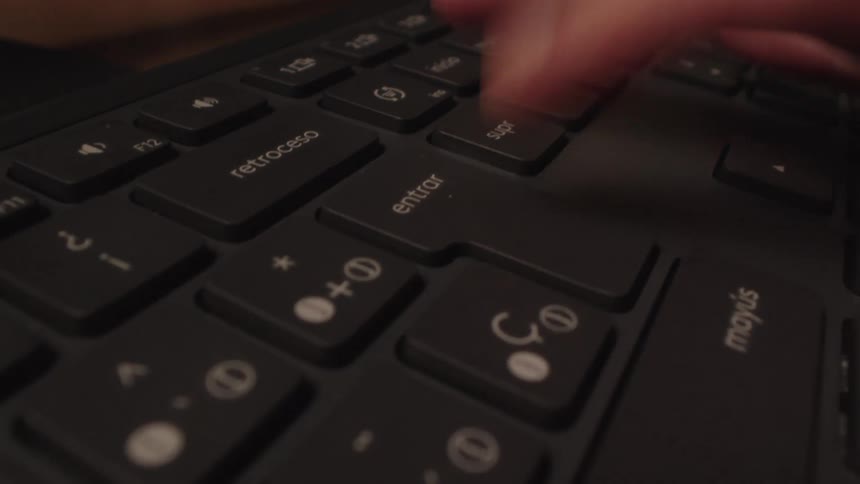 A dramatic close-up of a person frantically typing on a Spanish keyboard before repeatedly pressing the 'enter' key