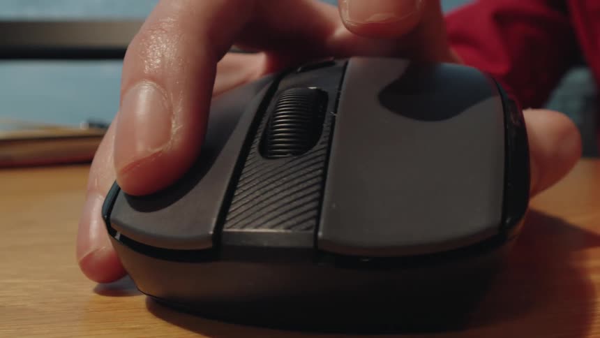 A macro close-up shot of a hand clicking and scrolling a wireless computer mouse on a desk