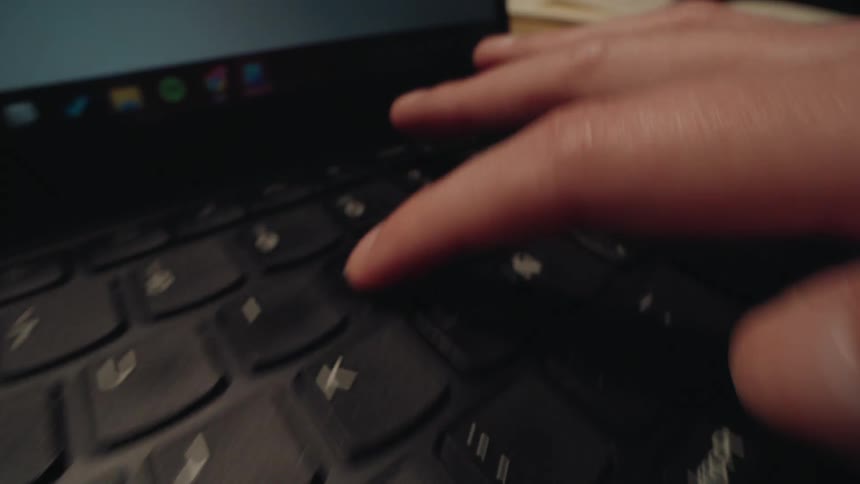 An extreme close-up shot captures a person typing on a laptop keyboard and finally pressing the enter key
