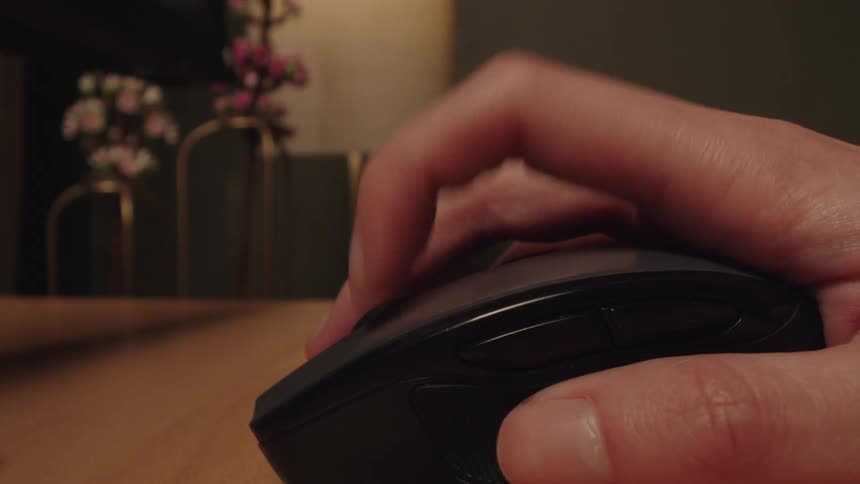 A close-up shot of a person's hand repeatedly clicking a computer mouse while working or browsing at a desk