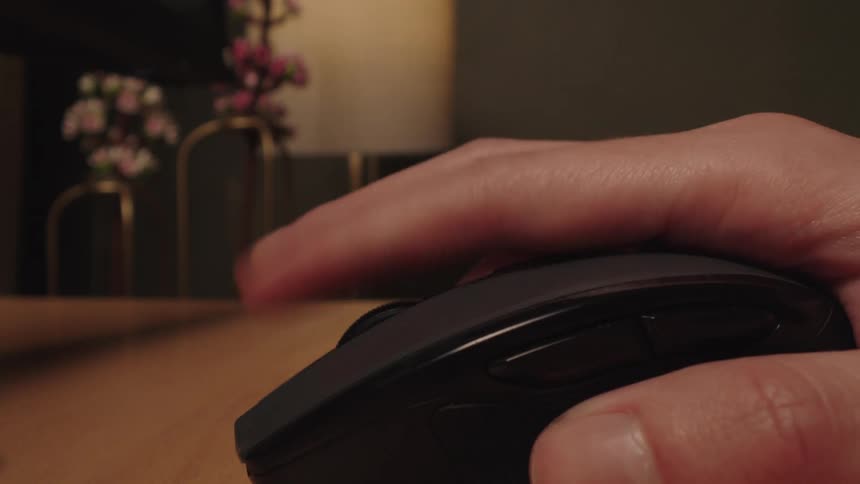 A person's hand scrolls and clicks on a wireless computer mouse while working at an office desk