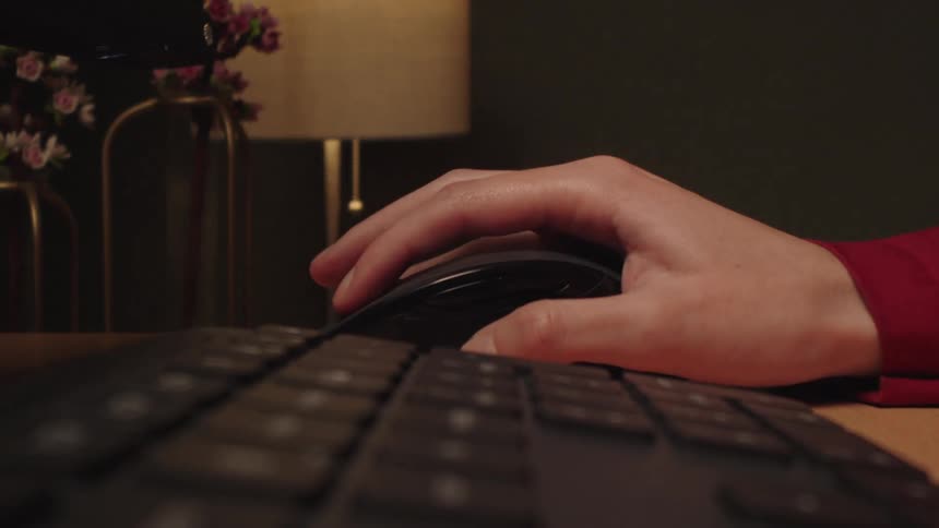 Close up of a hand clicking and scrolling on a computer mouse at a desk in a dimly lit room