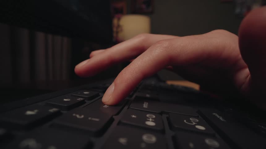 Extreme close-up of a finger pressing a key on a computer keyboard in a dimly lit room at night