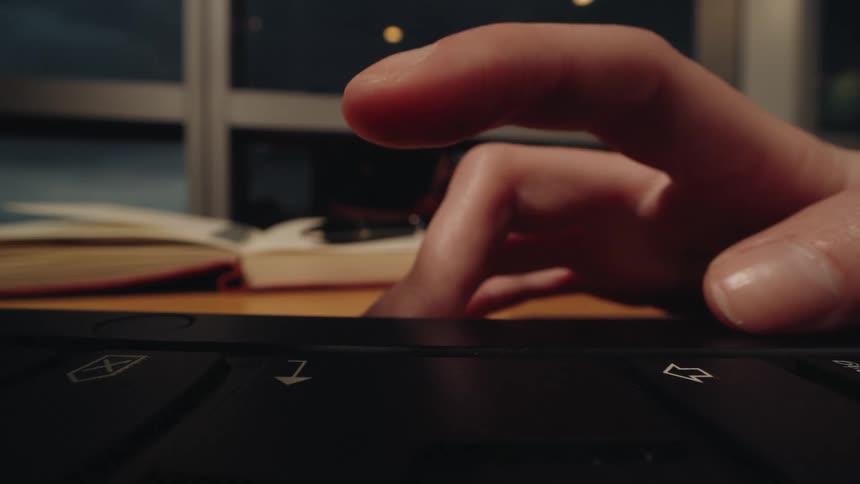 A macro shot of a person's finger tapping and scrolling on a laptop trackpad at a desk late at night