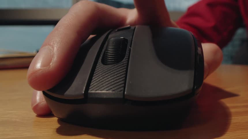 A close-up dolly shot of a person's hand clicking a wireless computer mouse on a desk