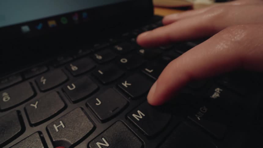 A close-up, macro shot of a person's fingers typing on a black laptop keyboard before pressing the enter key