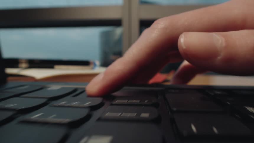 A dynamic macro shot tracks along a black laptop keyboard as fingers type rapidly, then pause
