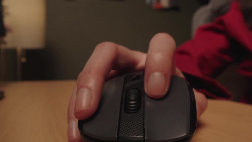 POV close-up of a hand frantically clicking and moving a wireless computer mouse on a wooden desk