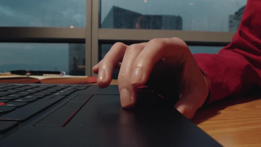 Detail shot of a hand using a laptop trackpad to work in a city office on a rainy day