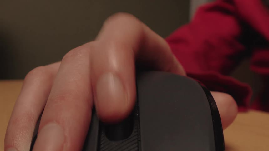 An extreme close-up shot of a person's finger clicking and scrolling on a black wireless computer mouse on a wooden desk