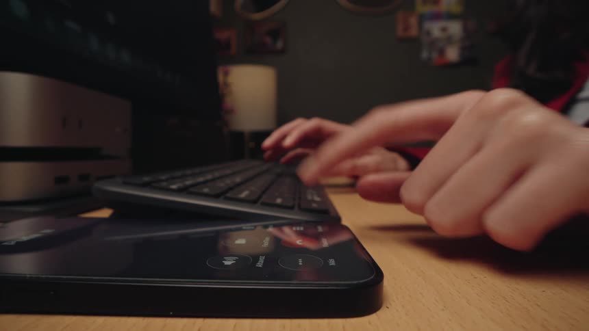 Close-up of a person typing on a keyboard, then answering an incoming phone call on speakerphone to continue working