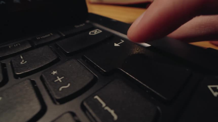 A dramatic close-up of a finger slowly pressing the enter key on a laptop keyboard