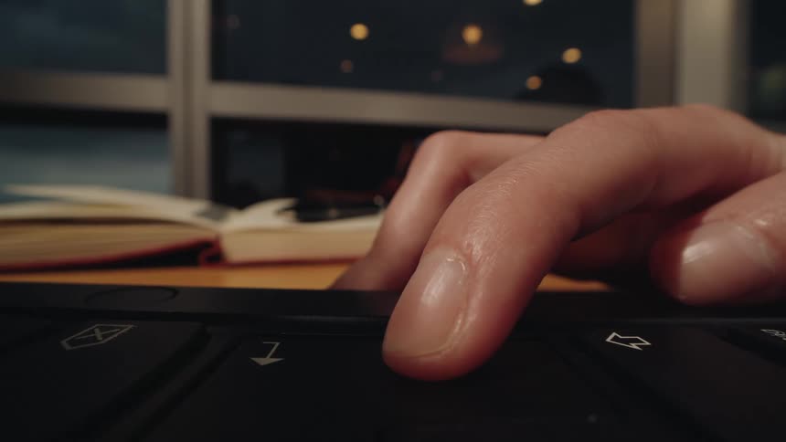 A macro shot of a finger repeatedly pressing the down arrow key on a keyboard while working at a desk at night