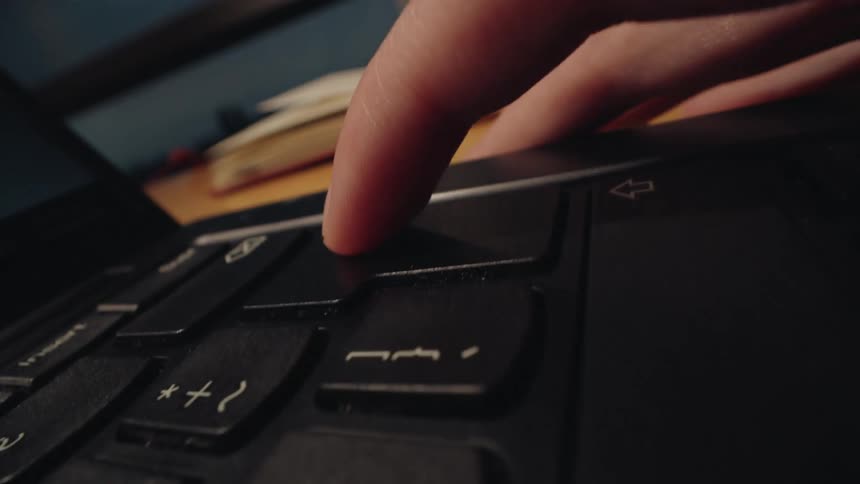 A dramatic macro close-up shows a finger slowly pressing the enter key on a black laptop keyboard