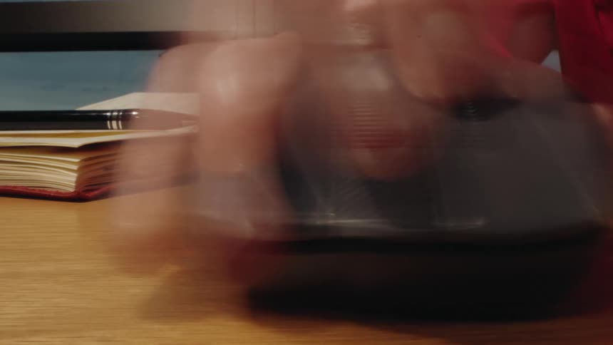 A stressful close-up timelapse of a hand frantically clicking and scrolling a wireless computer mouse on a desk