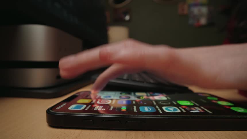 Dynamic close-up reveals a person multitasking, typing on a keyboard and then opening the Amazon app on their smartphone
