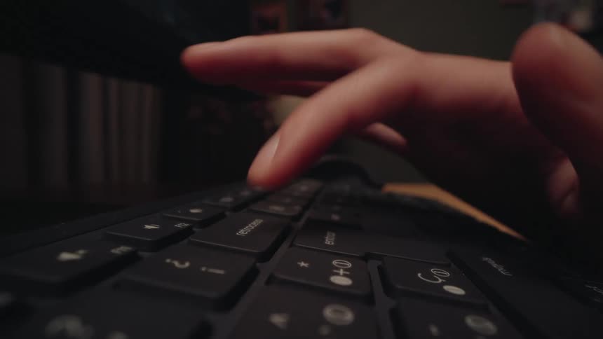 A dramatic close-up shot of a hand repeatedly pressing the backspace key on a computer keyboard in a dimly lit room