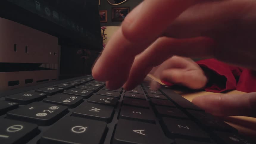 A frantic time-lapse close-up of a person's hands typing quickly on a computer keyboard in a dimly lit office