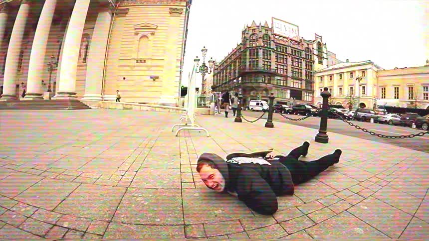 A skateboarder in a black hoodie comically fails a trick in slow motion and crawls away on the ground in a city square