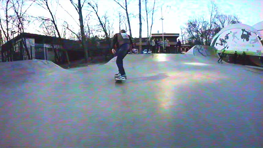 Slow-motion footage with a retro VHS effect of a skateboarder performing tricks at an outdoor skatepark