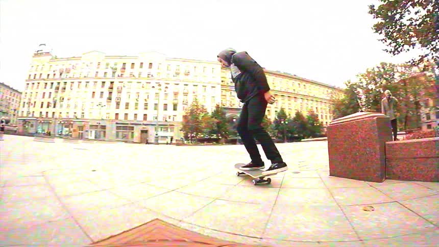 Retro VHS-style slow-motion footage of a skateboarder grinding a ledge and landing a kickflip in a city square
