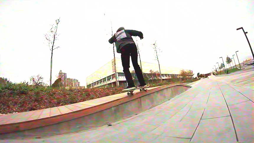 A skateboarder in a black hoodie grinds along a curved ledge in a modern city park in slow motion with lo-fi VHS effects