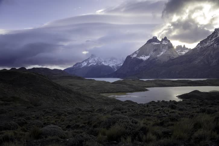 A moody timelapse of rolling clouds over the snow-capped mountain peaks and tranquil lake in Patagonia's wilderness