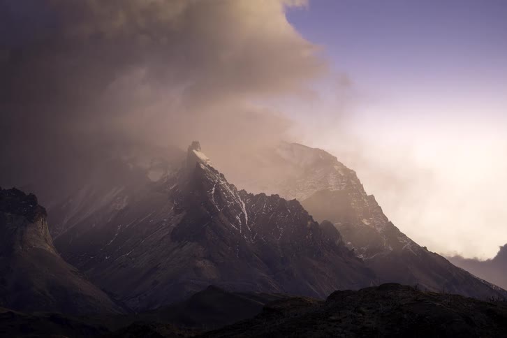 A dramatic time-lapse captures moody storm clouds moving across majestic, snow-capped mountains illuminated by soft light