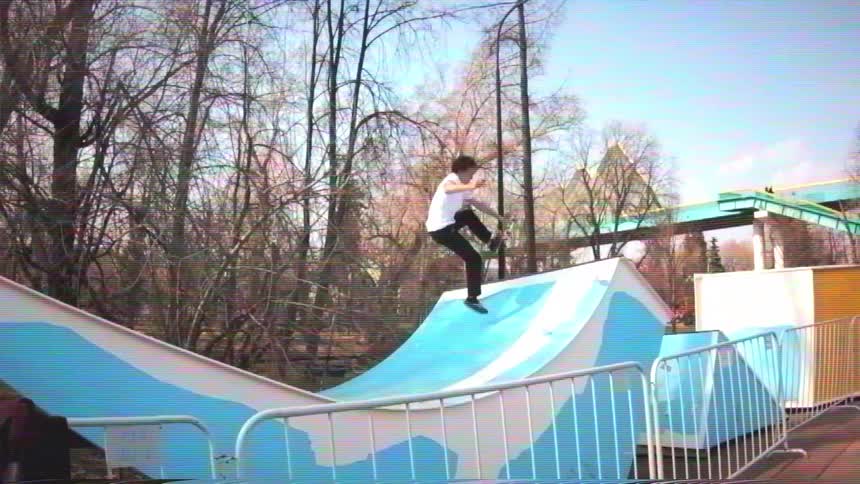 Slow motion of a skater dropping into a small, wave-like ramp and performing an ollie in a park, filmed in a retro VHS style