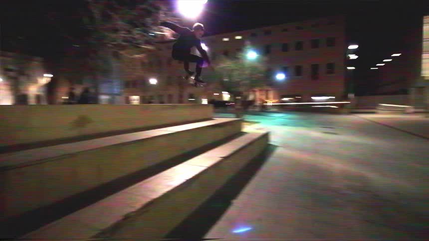 A skateboarder dramatically falls in slow motion after attempting to jump a set of stairs at night in a city plaza